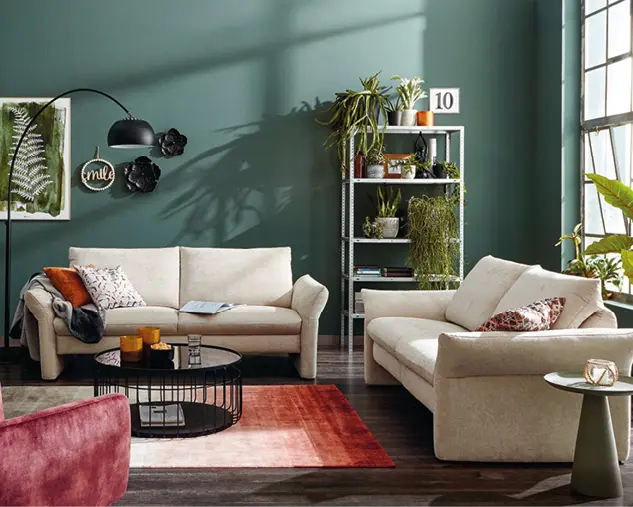 Gemütliches Wohnzimmer mit zwei beigen Sofas, rundem Couchtisch und Teppich in warmen Farben. Moderne Wohnlandschaft mit dekorativen Kissen, Regal und stilvoller Einrichtung für entspanntes Wohnen.